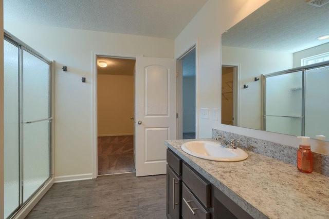 full bathroom featuring a textured ceiling, vanity, a spacious closet, wood finished floors, and a stall shower