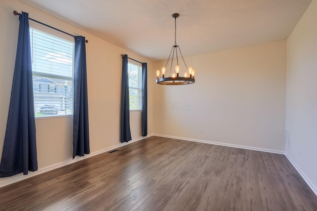 spare room with a wealth of natural light, an inviting chandelier, and dark wood finished floors