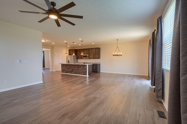 unfurnished living room featuring dark wood-type flooring, ceiling fan with notable chandelier, baseboards, and visible vents