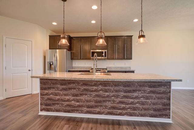 kitchen with baseboards, dark wood-style flooring, a kitchen island with sink, dark brown cabinets, and stainless steel appliances
