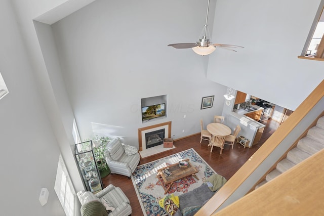 living room with a towering ceiling, stairs, a fireplace with flush hearth, ceiling fan, and wood finished floors