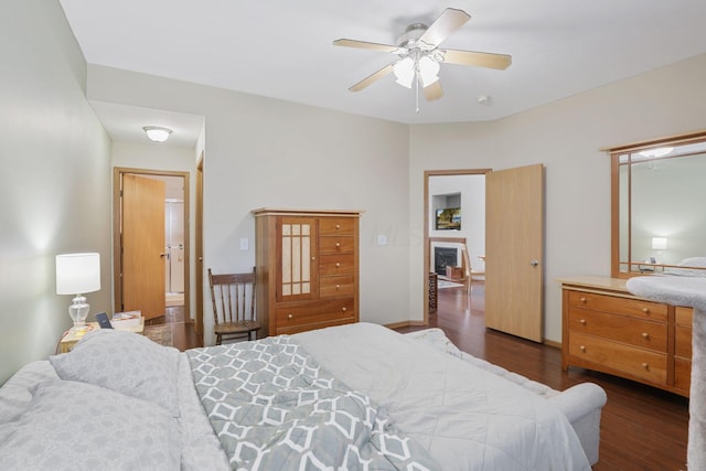 bedroom with a fireplace, ceiling fan, and dark wood finished floors