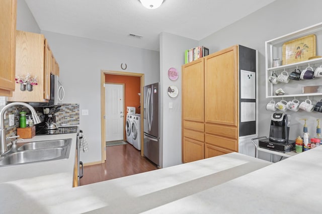 kitchen featuring tasteful backsplash, appliances with stainless steel finishes, a sink, light countertops, and washer and dryer