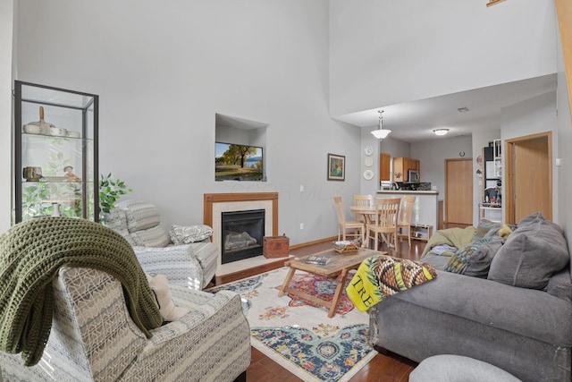 living area featuring a fireplace with flush hearth, wood finished floors, a high ceiling, and baseboards