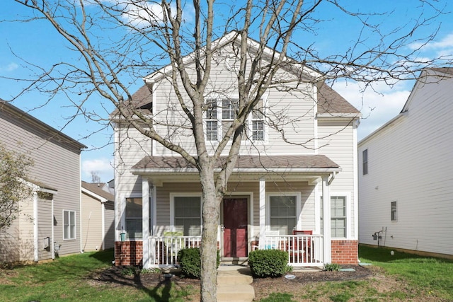 view of front of property featuring roof with shingles, covered porch, a front yard, and brick siding