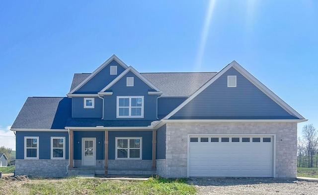 craftsman-style house featuring a garage, gravel driveway, a porch, and stone siding