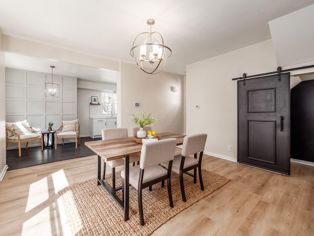 dining room with a barn door, light wood-style flooring, baseboards, and an inviting chandelier