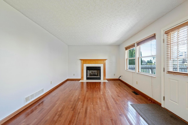 unfurnished living room featuring a tile fireplace, light wood finished floors, visible vents, and baseboards