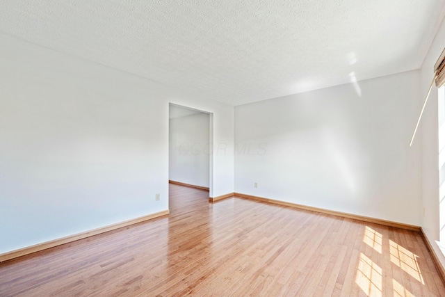 spare room featuring light wood-style flooring, a textured ceiling, and baseboards