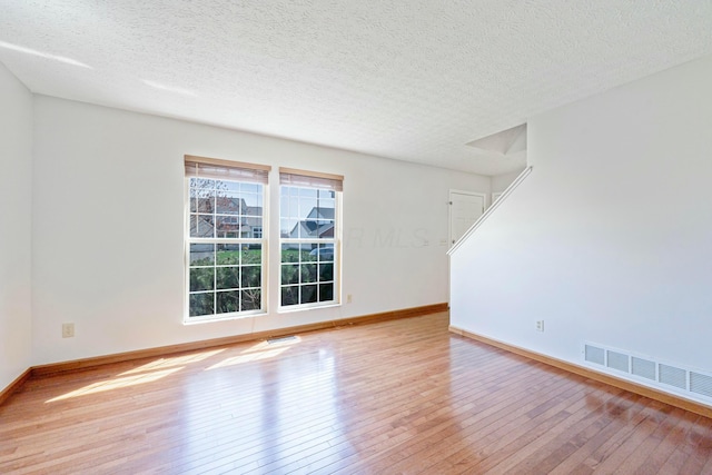 empty room with visible vents, baseboards, hardwood / wood-style flooring, and a textured ceiling