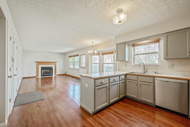 kitchen featuring a peninsula, dishwasher, a sink, gray cabinetry, and hardwood / wood-style flooring