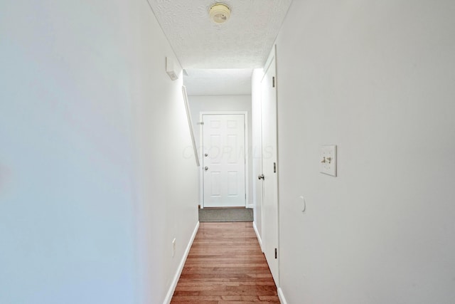 hallway with a textured ceiling, baseboards, and wood finished floors