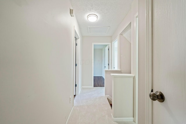 hallway featuring carpet flooring, attic access, a textured ceiling, and baseboards