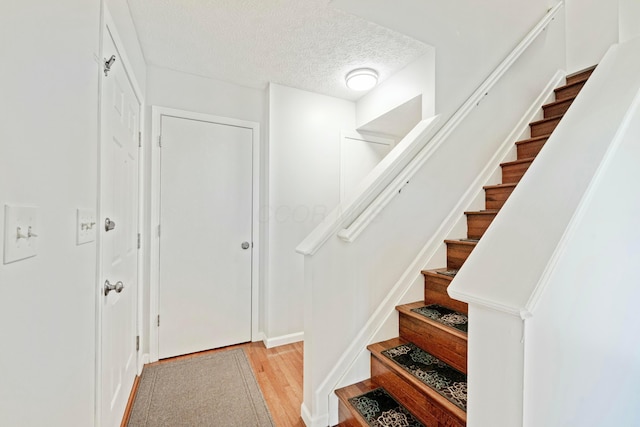 staircase with a textured ceiling and wood finished floors