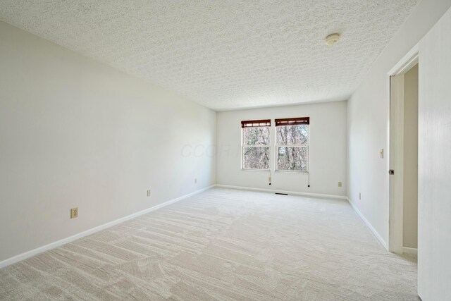 unfurnished room featuring light carpet, baseboards, and a textured ceiling