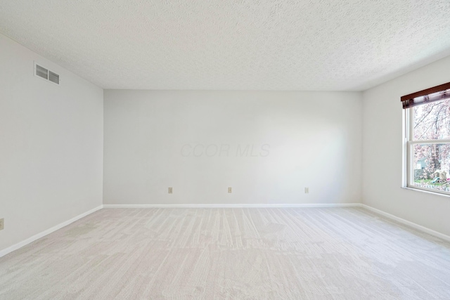 spare room with light carpet, visible vents, baseboards, and a textured ceiling