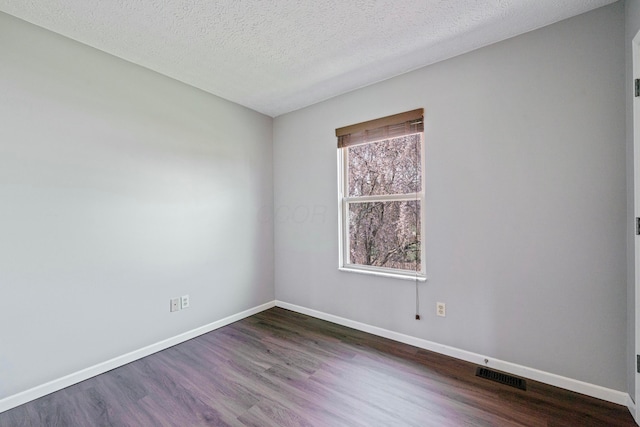 empty room featuring a textured ceiling, baseboards, dark wood-style floors, and visible vents