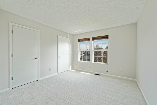 unfurnished bedroom with a textured ceiling, carpet flooring, baseboards, and visible vents