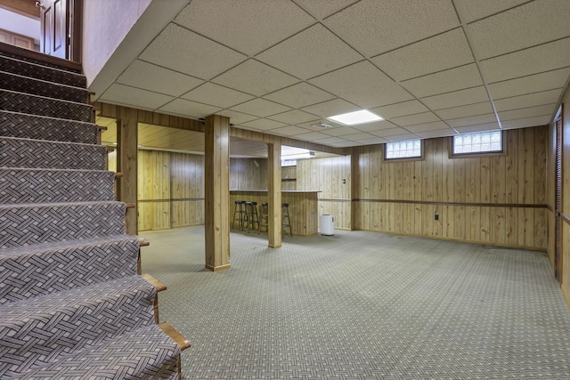 below grade area featuring wooden walls, carpet flooring, baseboards, a drop ceiling, and stairway