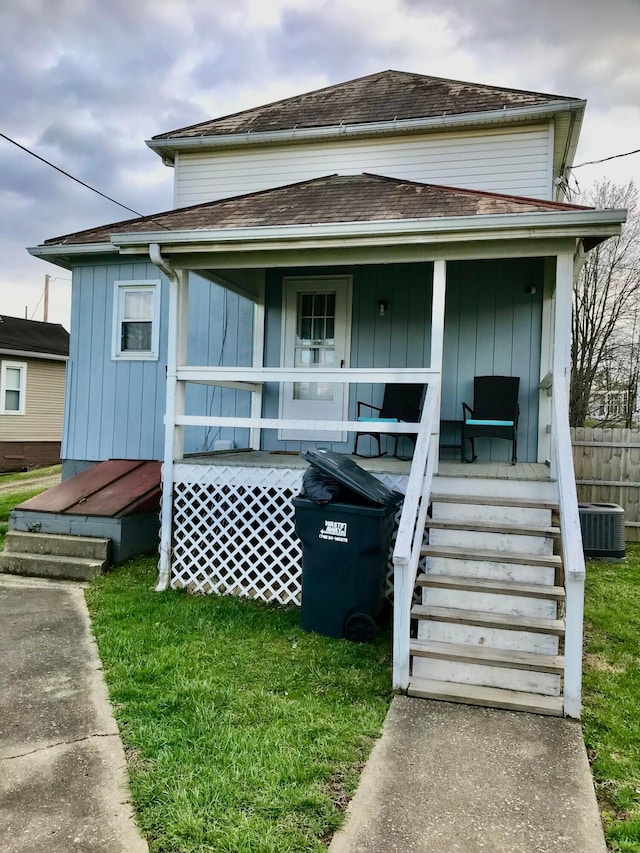 view of front of home with roof with shingles, a front yard, central AC unit, fence, and covered porch