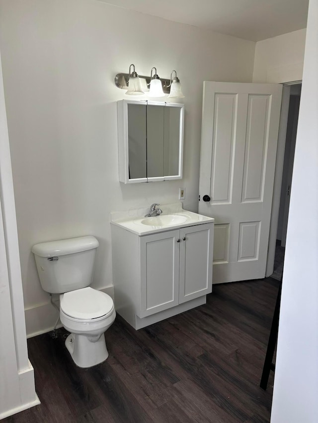 half bathroom with toilet, wood finished floors, vanity, and baseboards