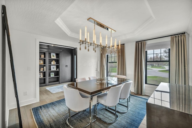 dining area with baseboards, a raised ceiling, built in shelves, and wood finished floors