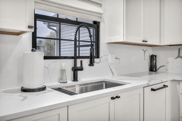 kitchen featuring light stone countertops, a sink, white cabinetry, and tasteful backsplash