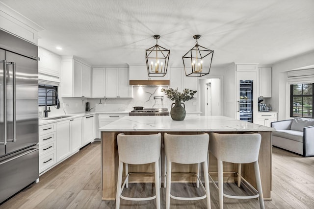 kitchen featuring an inviting chandelier, built in fridge, white cabinets, dishwasher, and a sink