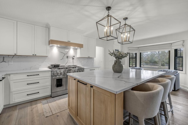 kitchen with light stone countertops, a chandelier, under cabinet range hood, range with two ovens, and a kitchen island