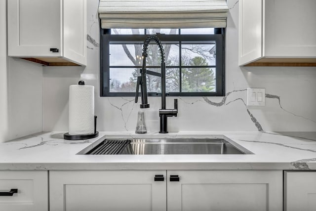 kitchen with light stone countertops, white cabinetry, decorative backsplash, and a sink