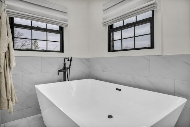 bathroom with plenty of natural light, a freestanding bath, and tile walls