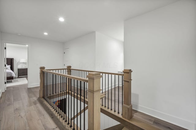 hall with an upstairs landing, wood finished floors, and baseboards