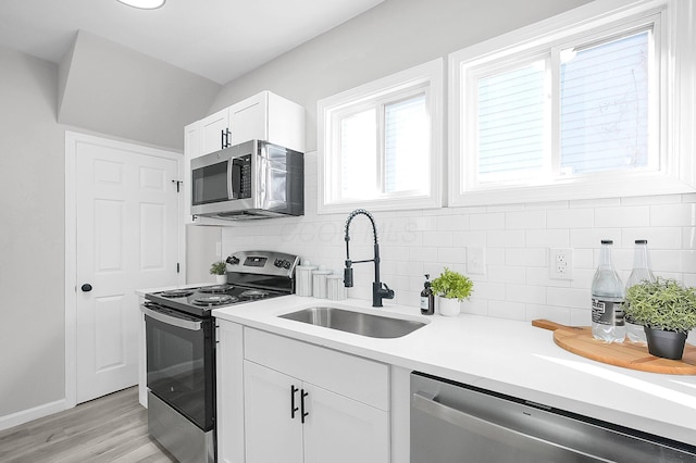 kitchen with appliances with stainless steel finishes, light countertops, white cabinets, decorative backsplash, and a sink