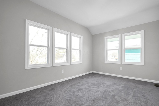 spare room featuring visible vents, baseboards, dark carpet, and lofted ceiling