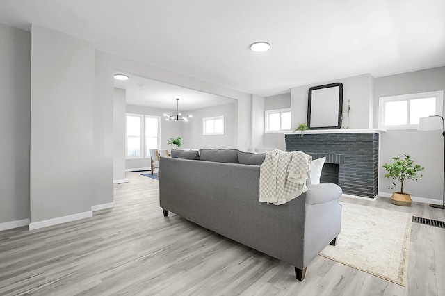 living room featuring light wood-style flooring, baseboards, a notable chandelier, and a fireplace