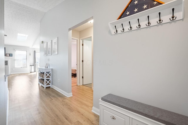 hall featuring light wood-type flooring, baseboards, lofted ceiling, and a textured ceiling