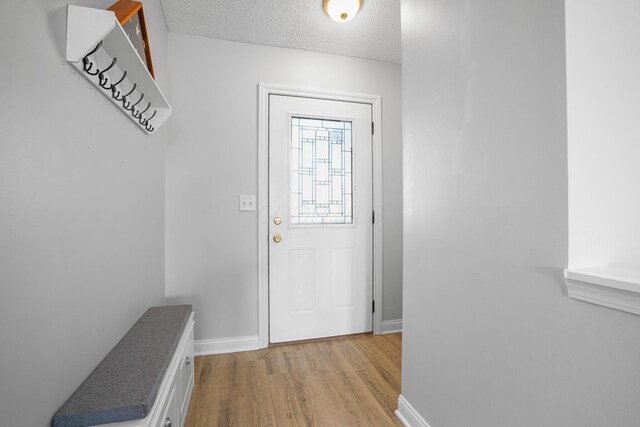 doorway featuring baseboards, light wood-type flooring, and a textured ceiling