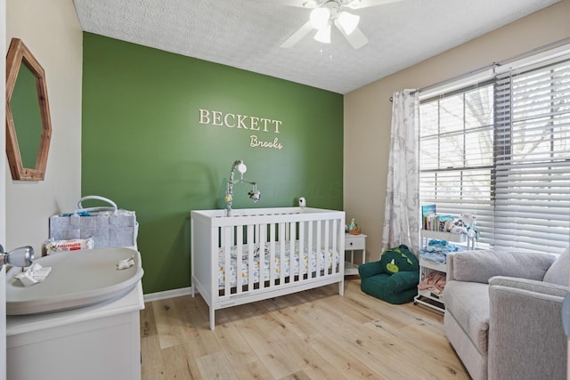 bedroom featuring baseboards, a crib, a textured ceiling, a sink, and wood finished floors