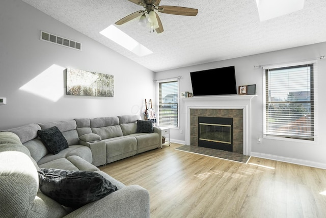 living room featuring visible vents, ceiling fan, vaulted ceiling with skylight, and wood finished floors