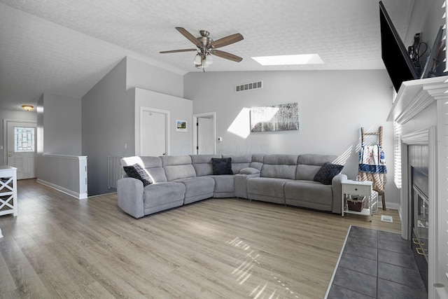living room with ceiling fan, a textured ceiling, visible vents, wood finished floors, and lofted ceiling with skylight
