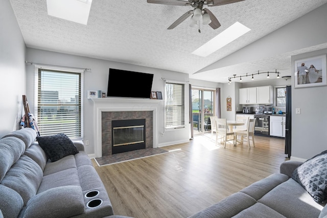 living room with ceiling fan, a textured ceiling, a fireplace, light wood finished floors, and lofted ceiling with skylight