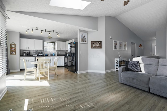 living room with light wood-type flooring, vaulted ceiling with skylight, and a textured ceiling