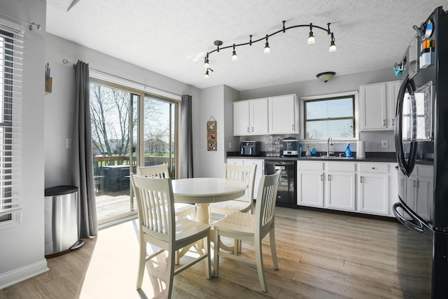 kitchen with dark countertops, freestanding refrigerator, white cabinetry, and light wood finished floors