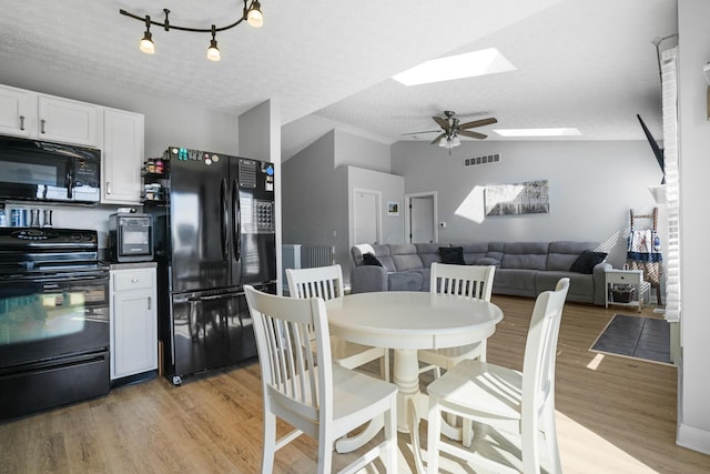 dining area featuring vaulted ceiling with skylight, a textured ceiling, visible vents, and light wood-style floors