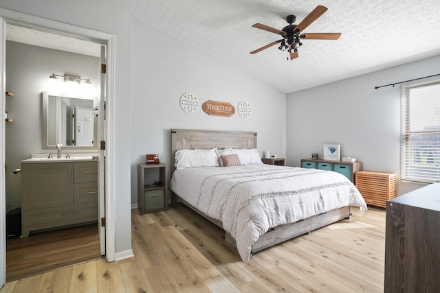 bedroom with light wood-type flooring, vaulted ceiling, a textured ceiling, connected bathroom, and a sink