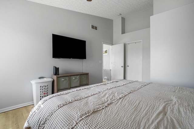 bedroom featuring high vaulted ceiling, a textured ceiling, visible vents, wood finished floors, and baseboards