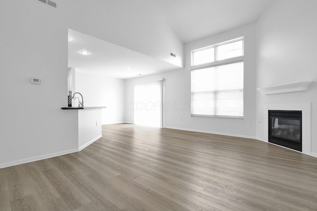 4899 Common Market Pl, Dublin, OH 43016 - unfurnished living room featuring wood finished floors, a tiled fireplace, healthy amount of natural light, and a high ceiling