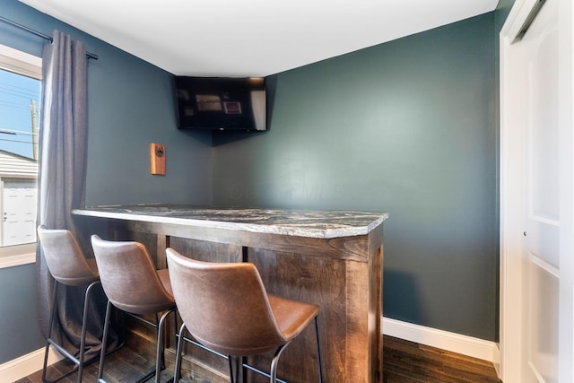bar featuring baseboards, a bar, and dark wood-style floors