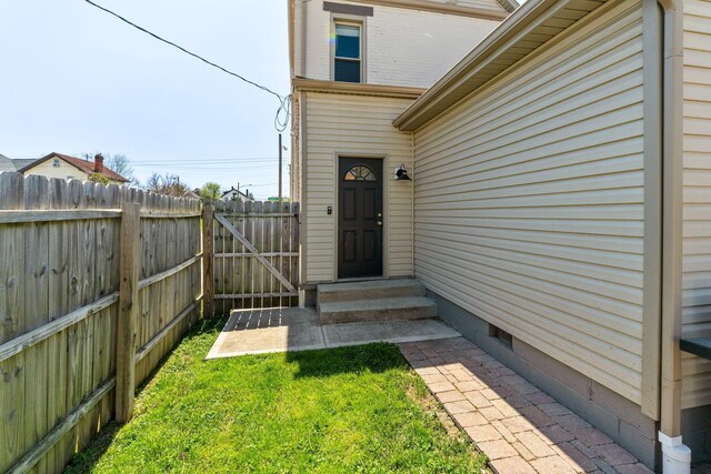 doorway to property with brick siding, fence, and a yard