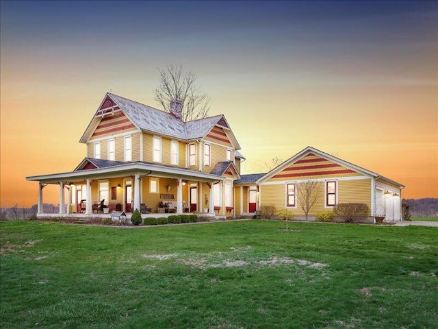 back of house at dusk featuring a porch, a lawn, and a garage